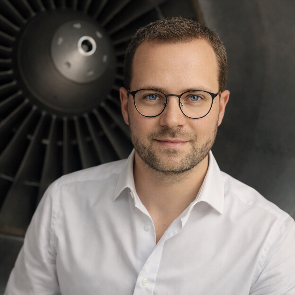 Mann mit Brille, lächelt vor einem großen Triebwerk.